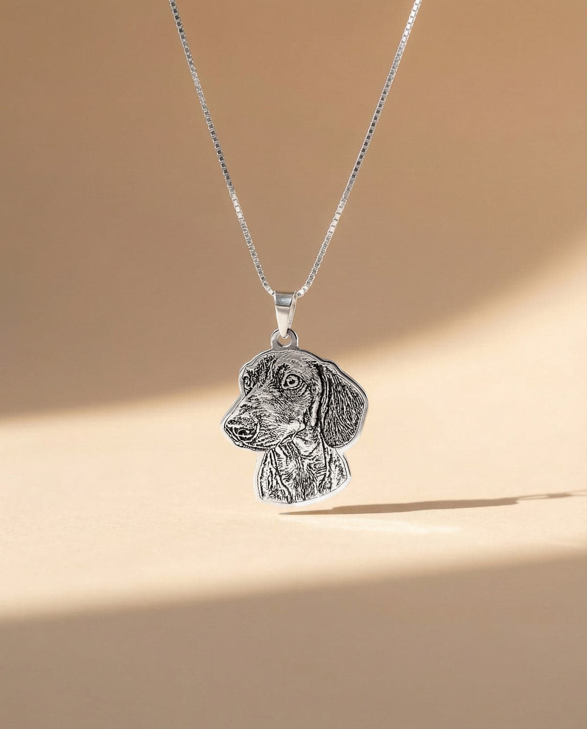 A sterling silver contour-cut pendant engraved with a dog portrait, on a box chain.